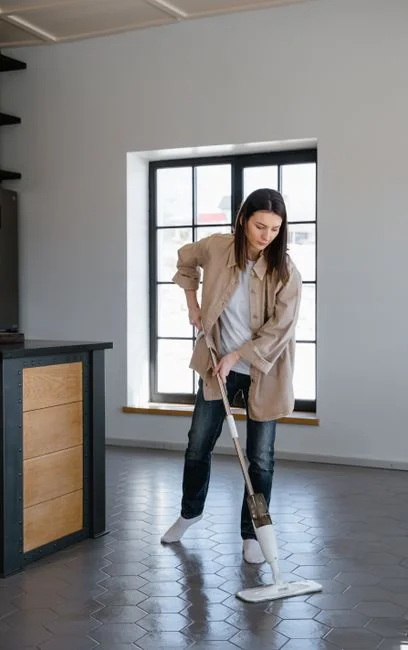 Two women in red overalls vacuuming and sweeping a modern living room.