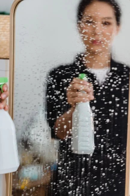 Two women in work clothes cleaning a modern living room using a vacuum and mop.